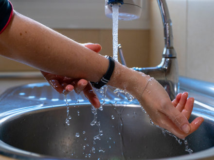 Das Bild zeigt die Hände und einen Unter·arm von einer Frau. Die Frau kühlt die Hände mit kaltem Wasser aus dem Wasserhahn.