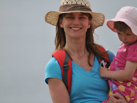 Das Bild zeigt eine Frau mit einem kleinen Mädchen auf dem Arm. Beide tragen einen Sonnen·hut.