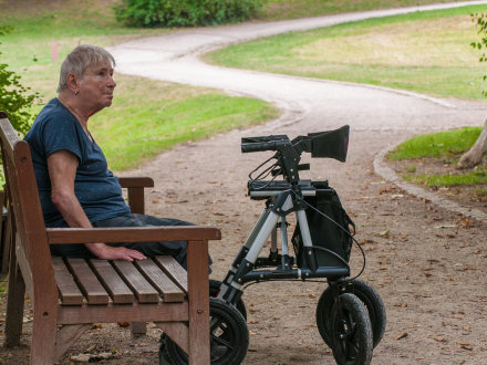 Das Bild zeigt eine ältere Frau auf einer Park·bank im Schatten.