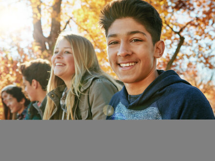 Bild © Grady Reese/peopleimages.com / stock.adobe Foto: 5 Jugendliche sitzen nebeneinander. Der Jugendliche ganz vorn lächelt in die Kamera. Die Jugendliche daneben lächelt auch. Die anderen 3 Jugendlichen unterhalten sich miteinander., Bild © Grady Reese/peopleimages.com / stock.adobe