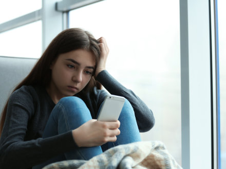 Das Bild zeigt ein trauriges Mädchen mit einem Handy in der Hand.