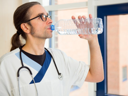 Das Bild zeigt einen Kranken·pfleger bei der Arbeit. Der Kranken·pfleger trinkt Wasser aus einer Flasche.