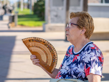 Das Bild zeigt eine ältere Frau mit einem Fächer im Sommer.