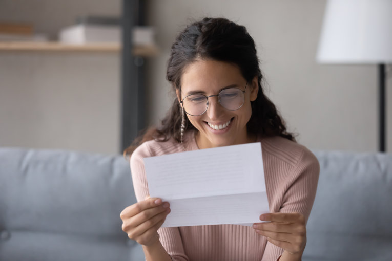 Das Bild zeigt eine lächelnde junge Frau mit einem Brief.