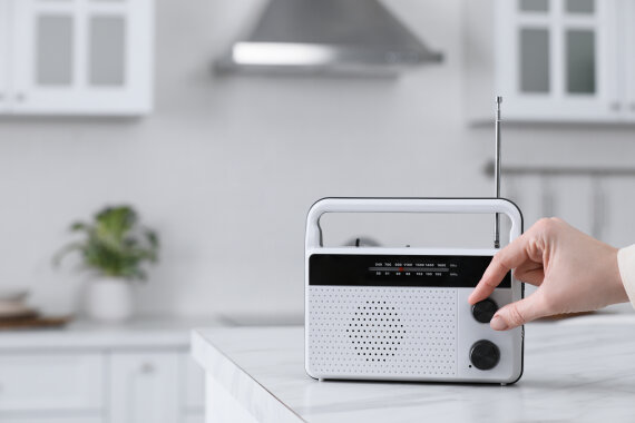 Foto von einem Radio·gerät auf einem Tisch. Eine Hand dreht an dem Knopf für die Laut·stärke.