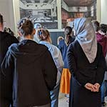 Eine Gruppe blickt auf ein aktuelles und ein historisches Foto des Saal 600.