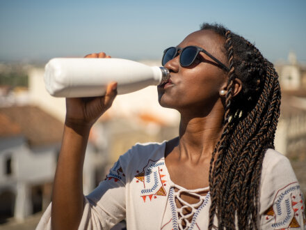 Foto von einer Frau mit einer Sonnen·brille und einer Flasche Trinken., Bild © MalaikaCasal / stock.adobe