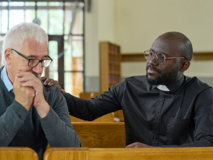 Foto von einem Pfarrer und einem älteren Mann. Der Pfarrer tröstet den älteren Mann., Bild © pressmaster / stock.adobe