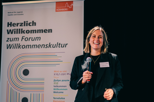 Katharina Schwartz mit Mikrofon in der Hand, im Hintergrund ein Roll-Up