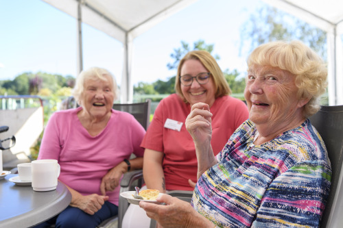 Seniorinnen essen mit Mitarbeiterin Kuchen auf der Terrasse