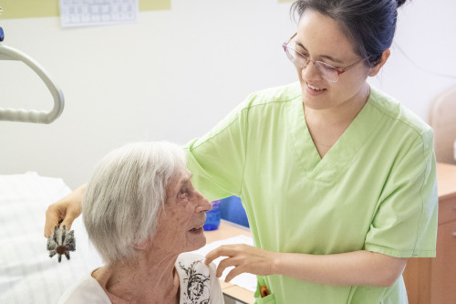 Pflegekraft kämmt Seniorin im Bett die Haare.