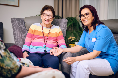 Pflegekraft und Seniorin sitzen im Wohnzimmer des August-Meier-Hauses
