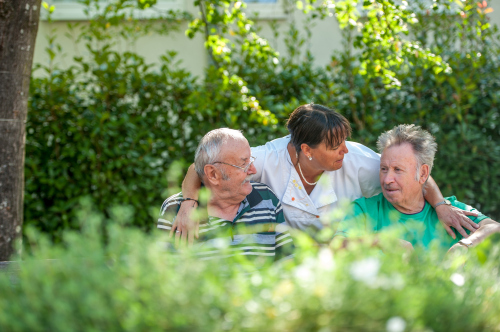 Zwei Senioren sitzen mit Pflegekraft im Park