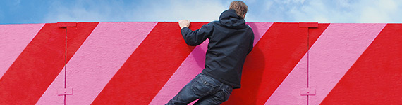 Ein junger Mann springt über eine bunt gestreifte Mauer