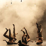 Mehrere Balletttänzer liegen mit in die Luft gestreckten Beinen auf dem Rücken