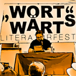 Ein Mann liest auf einer Bühne aus einem Buch. Darüber der Text: "WortWärts. Literaturfest".