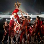 Rot gekleidete Ballett-Tänzerinnen und -Tänzer heben eine Tänzerin in die Luft