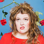 Eine Frau mit zerzaustem Haar, blick zerknirscht nach oben. Aus dem Himmel fallen viele rote Rosen auf sie herab.