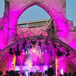 Eine bunt angestrahlte Musikbühne im Inneren der Katharinenruine mit Publikum