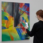Eine Frau steht vor einem Gemälde von Gerhard Richter. Dabei hält sie ein Smartphone in Hand und betrachtet weitere Informationen zu dem Gemälde.