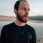 Mann mit Vollbart und nassen Haaren und Kleidung am Strand