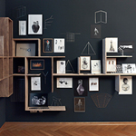 Ein Kunstwerk mit einer dunklen Wand, an der geometrische Holzregale und Bilder in unterschiedlichen Formaten angebracht sind. Die Collagen und Zeichnungen zeigen surreal anmutende Figuren, Objekte und abstrakte Formen, ergänzt durch filigrane Drahtstrukturen.