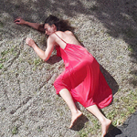 Barfüßige Person in rotem Kleid liegt auf einer Kiesfläche, Körper seitlich ausgestreckt.