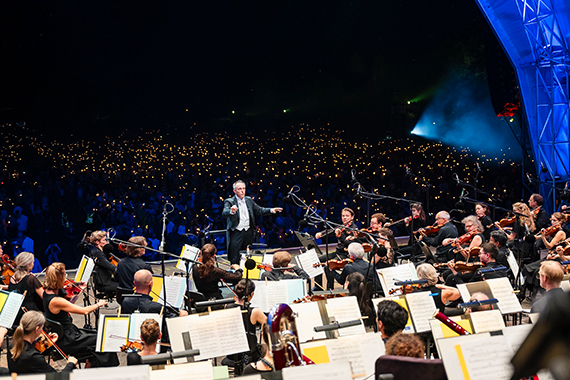 Ein Orchester steht auf einer bunt beleuchteten Konzertbühne beim Klassik Open Air.