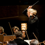 Dirigentin mit erhobenem Taktstock vor einem Orchester