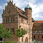 Historisches Sandsteingebäude mit Türmchen und Fachwerkhaus vor einem blauem Himmel