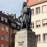 Statue von Albrecht Dürer auf einem hohen Sockel vor historischen mehrstöckigen Gebäuden mit Satteldächern