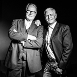 Zwei Männer stehen nebeneinander vor dunklem Hintergrund