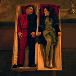 Zwei Personen liegen nebeneinander in offenen Särgen