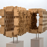 Holzskulptur mit rechteckiger Form und durchlöchertem, zerfressen wirkendem Mittelteil auf zwei Metallstangen