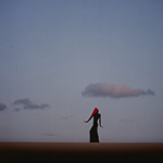 Silhouette einer Person mit rotem Kopftuch und langem Kleid vor einem Himmel mit wenigen Wolken