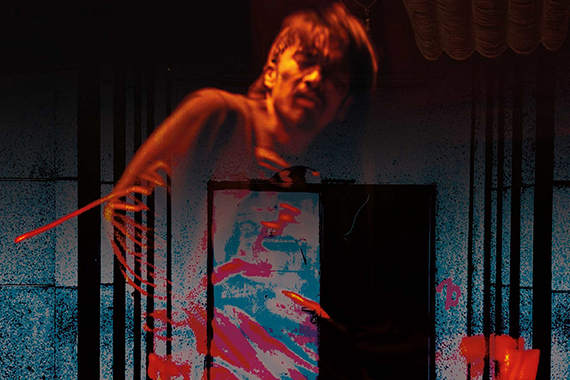 Person in weiter Hose und T-Shirt in dynamischer Pose in einem dunklen, verlassenen Raum mit Säulen und Tür im Hintergrund.