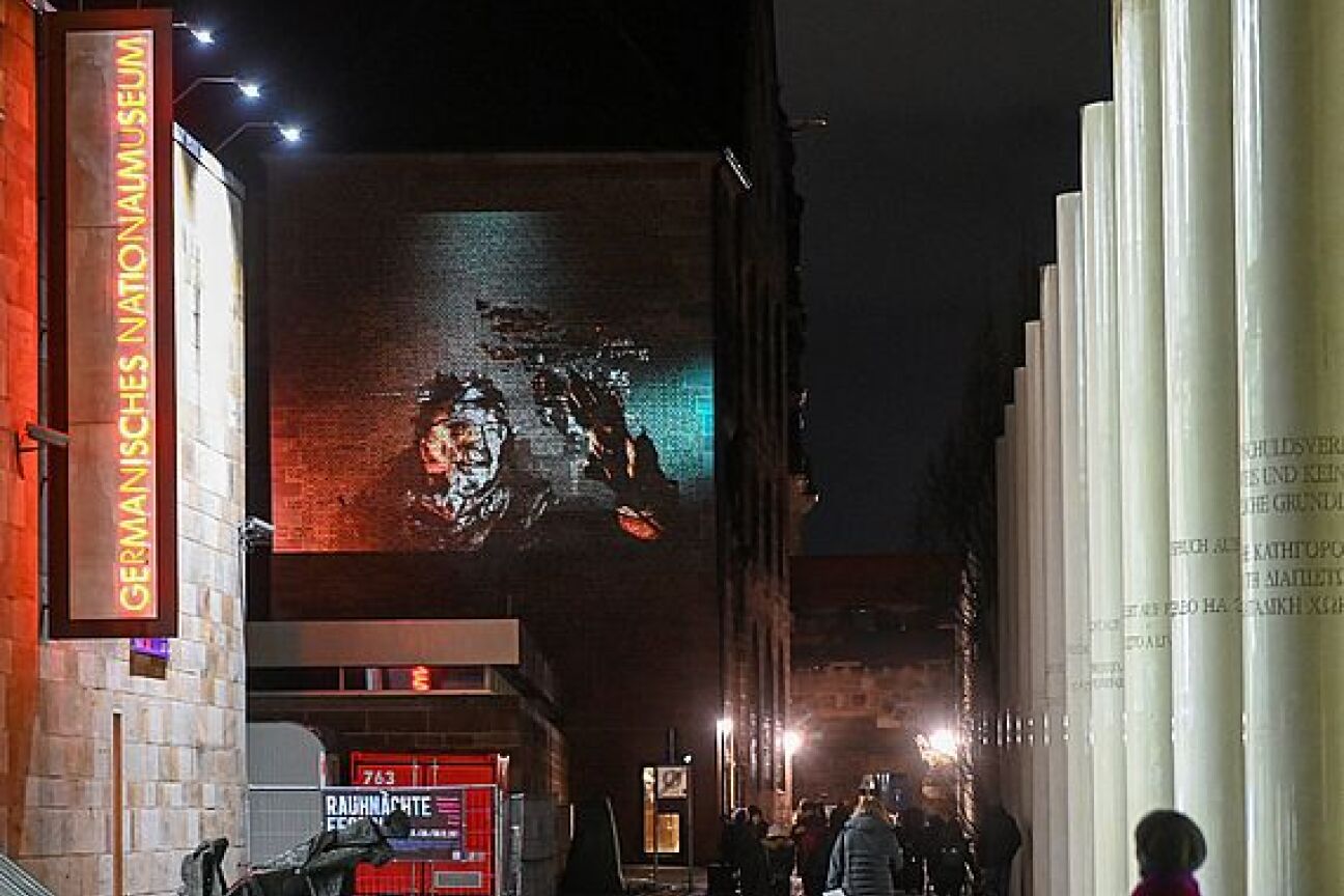 12|21 von elektropastete, Bild © Berny Meyer / Veroeffentlichung nur nach vorheriger Vereinbarung Der Kopf eines Mannes mit Brille und Bart ist verzerrt auf eine große Ziegelwand beim GNM projiziert, Bild © Berny Meyer / Veroeffentlichung nur nach vorheriger Vereinbarung