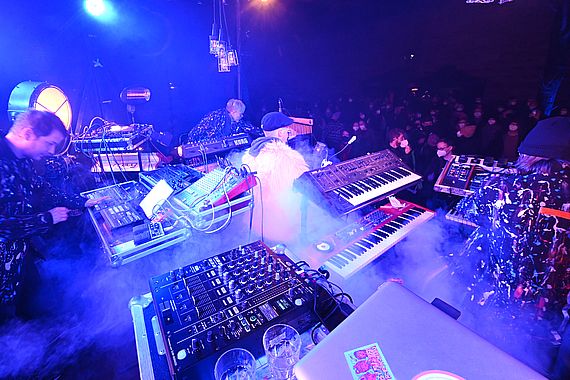 Die blaue beleuchtete Bühne ist voll mit der Japanischen Clubjacke und ihren Synthesizern