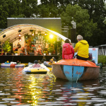 Das Publikum schwimmt auf Booten im Abend- und Bühnenlicht vor der Seebühne