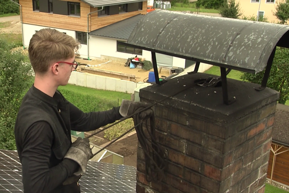Ein Schornsteinfeger reinigt einen Kamin auf dem Dach