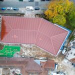 Aus der Vogelperspektive: Auf der gesamten Dachfläche des Schulneubaus sind rote Indach-Photovoltaikmodule in der Reutersbrunnenstraße 14 verbaut, um diese farblich in die umgebene Dachlandschaft einzuordnen.