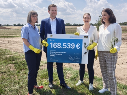 Foto: 4 Personen stehen neben einem Feld. 2 von den Personen halten ein Schild in der Hand. Alle Personen haben gelbe Gummi·handschuhe an. 3 Personen haben auch noch eine kleine Pflanze in der Hand., Bild © Edda Witthuhn / Stadt Nürnberg
