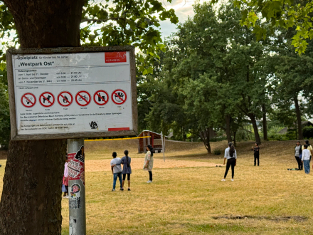 Foto vom West·park. Auf der Wiese stehen ein paar Menschen.