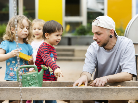 Bild © Uwe Niklas / Stadt Nürnberg Foto: Ein Erzieher aus einer Nürnberger Kita spielt mit Kindern im Sand·kasten., Bild © Uwe Niklas / Stadt Nürnberg
