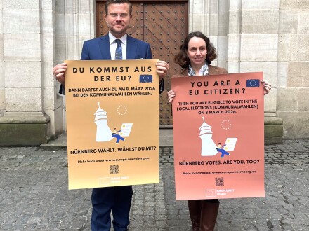 Foto vom Ober·bürgermeister Marcus König und Andrea Heilmaier. Andrea Heilmaier ist die Referentin für Wirtschaft und Wissenschaft von der Stadt Nürnberg. Beide halten Plakate zu den Info·veranstaltungen für EU-Bürger zur Kommunal·wahl in den Händen., Bild © C. Jekel / Europabüro der Stadt Nürnberg mit EUROPE DIRECT Nürnberg