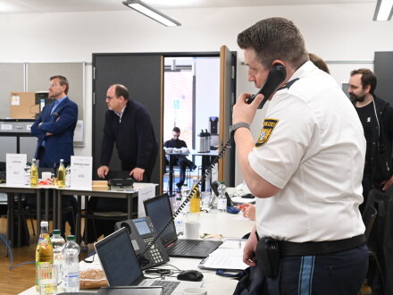 Foto von einem Zimmer mit vielen Personen. Eine Person von der Polizeit telefoniert. Andere stehen neben Tischen mit Laptops., Bild © Christine Dierenbach / Stadt Nürnberg