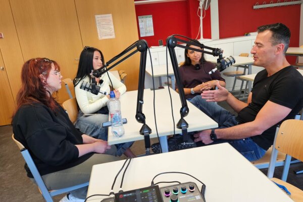 Foto: Die Schülerinnen Dilara, Leona und Vanessa bei der Aufzeichnung der neuen Podcast-Folge Bildungs·helden on Air in einem Klassenzimmer der Beruflichen Schule 9 mit dem Lehrer Serhat Gökce.