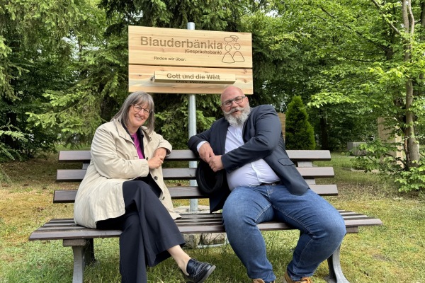 Britta Walthelm, Referentin für Umwelt und Gesundheit der Stadt Nürnberg, und Armin Hoffmann, Leiter der Friedhofsverwaltung, auf dem „Blauderbänkla" am Südfriedhof. Die Gesprächsbank steht allen Interessierten offen und lädt unkompliziert zu einem Gespräch ein.