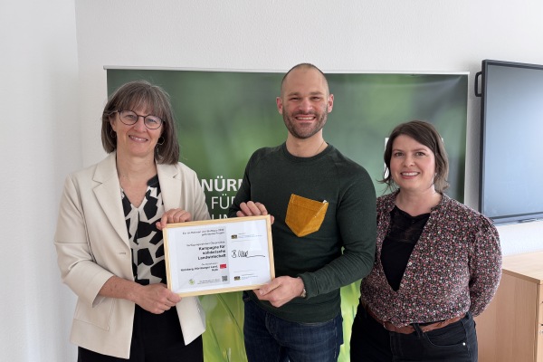 Britta Walthelm, Referentin für Umwelt und Gesundheit der Stadt Nürnberg, (links) übergab am Dienstag, 21. April 2026, Sebastian Lades und Monique Schindhelm das Förderschild für ihr Projekt der „SoLaWi Stadt, Land, Beides e. V.“, einer Initiative für solidarische Landwirtschaft in der Metropolregion Nürnberg.