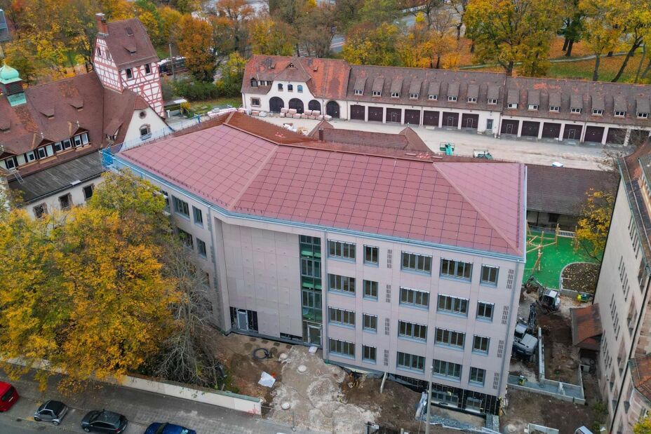 Auf der gesamten Dachfläche des Schulneubaus in der Reutersbrunnenstraße 14 sind rote Indach-Photovoltaikmodule verbaut, um diese farblich in die umgebene Dachlandschaft einzuordnen., Bild © Firma Bauer Energietechnik e.K.